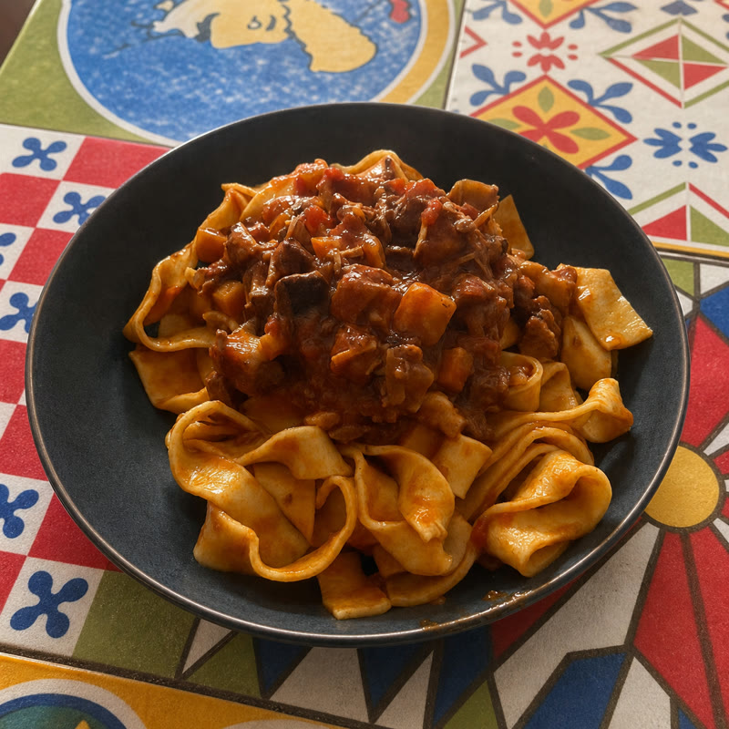 Pappardelle al ragù servite su piastrelle dipinte a mano