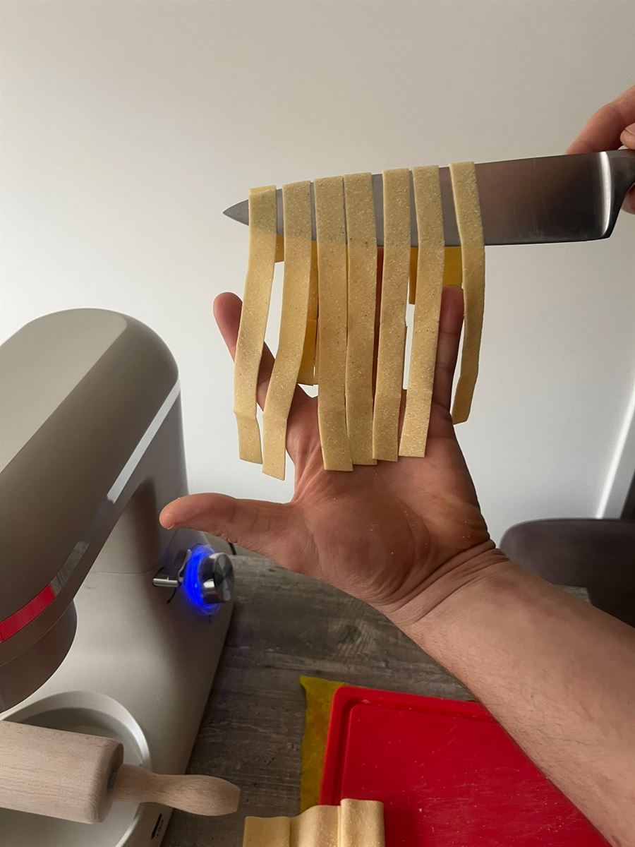 Pappardelle fresche appena tagliate, sollevate sulla lama del coltello